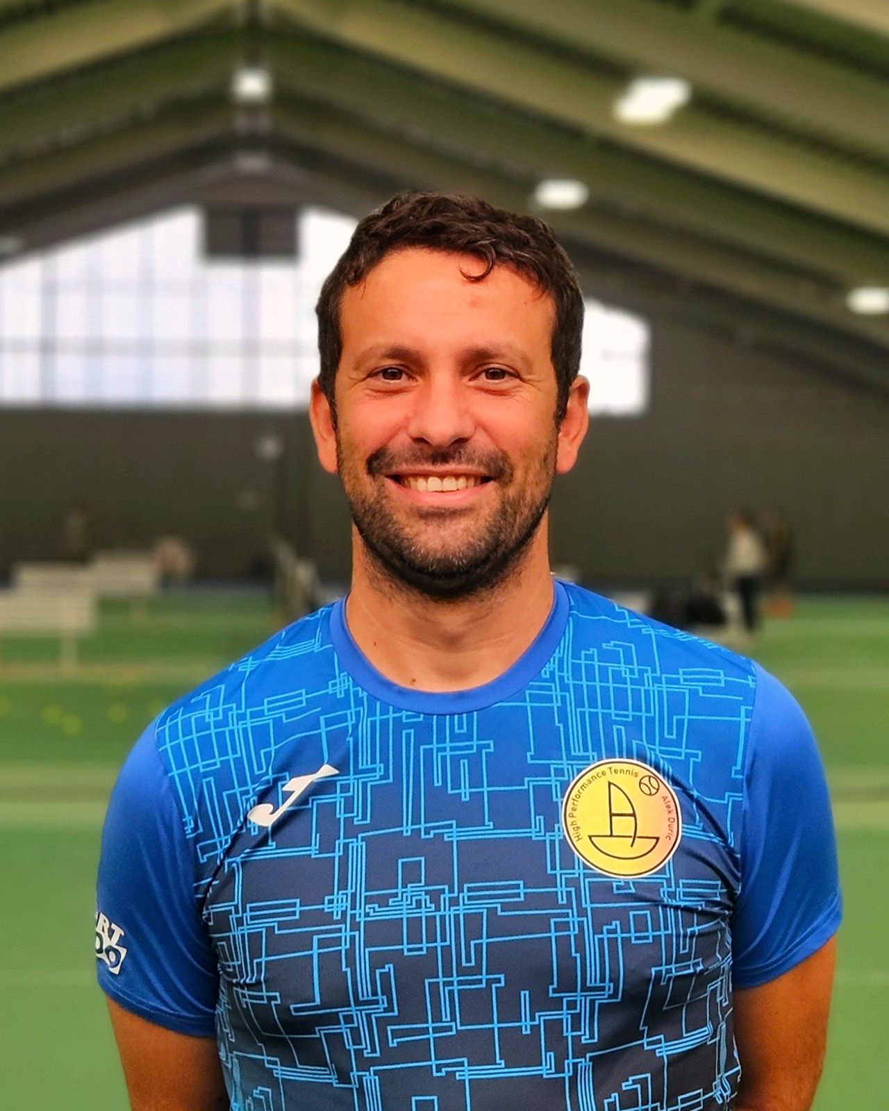 Alek Đurić, Head Coach, lächelnd im blauen Trainingsshirt in der Tennishalle